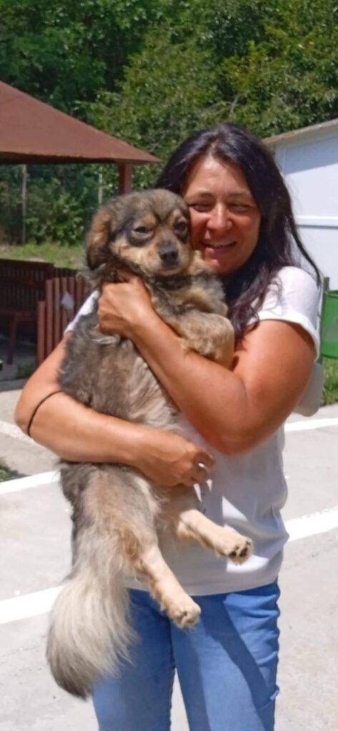 Frau mit weißem Shirt hält geretteten Hund Urban auf dem Arm und drückt ihn und lächelt fröhlich